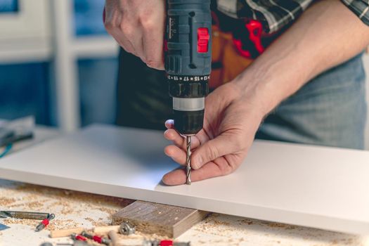 Man working making holes in board with drill during process of furniture manufacturing