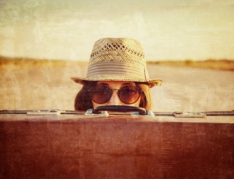 Hipster woman in hat and glasses looks out from vintage suitcase. Vintage image