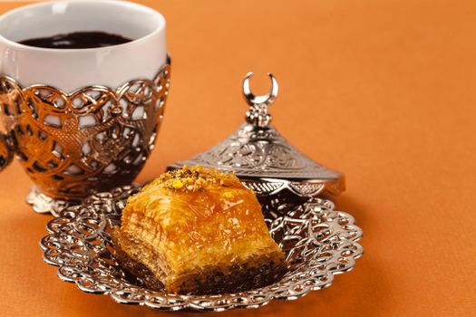 Turkish dessert baklava served on traditional metal tableware on orange background
