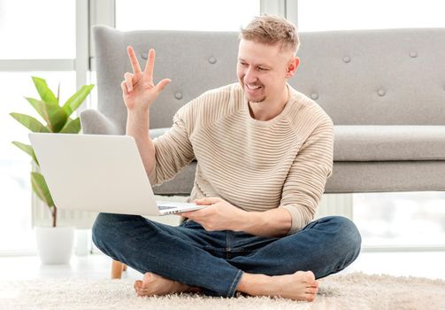 Man freelancer talking online using webcam on laptop during remote conference business call. Adult blond guy sitting on the floor and communicate with friends with camera