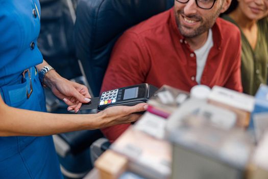 Close up shot of airline stewardess holding terminal while cheerful male passenger making payment. Travel, service, transportation, airplane concept