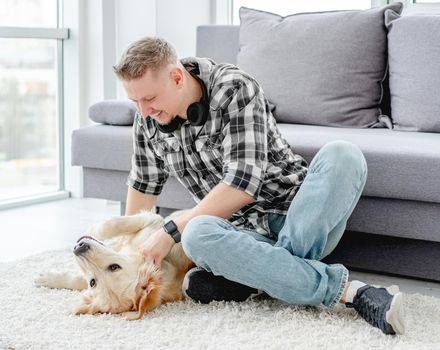 Happy man palming lovely dog on floor in light apartment