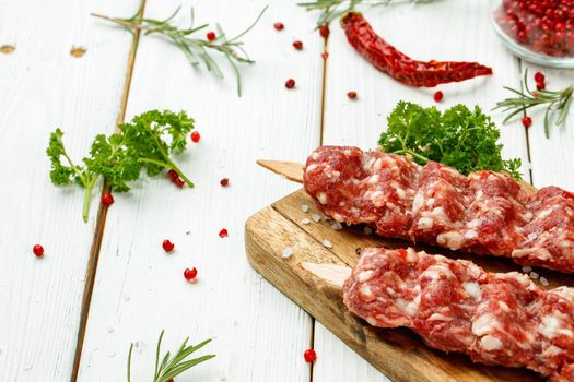Raw lula kebab on skewers with spices on wooden board close up