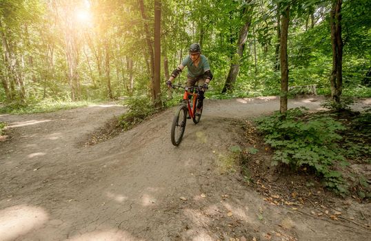 Man riding bicycle on forest road in shadows of high trees