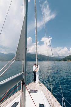 The bride and groom are hugging while standing on the bow of a white yacht sailing in the Bay of Kotor . High quality photo