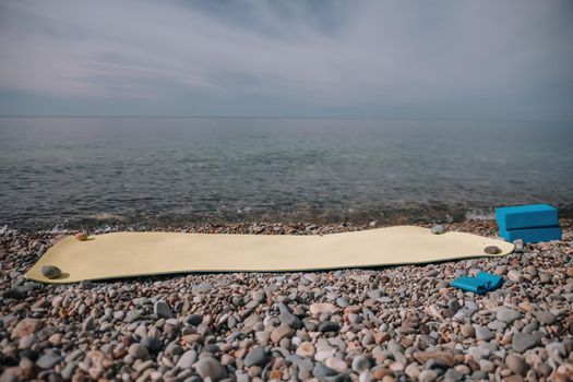 Young woman in swimsuit with long hair practicing stretching outdoors on yoga mat by the sea on a sunny day. Women's yoga fitness pilates routine. Healthy lifestyle, harmony and meditation concept.