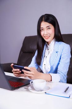 young business woman sitting at the desk with laptop and using mobile phone