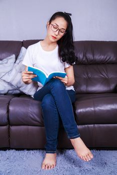 young woman reading a book on sofa at home