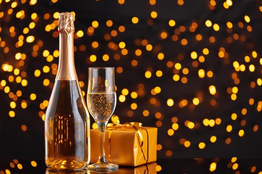 Champagne bottle and wrapped gift on blurred background of Christmas lights front view