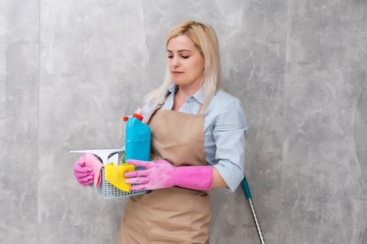 Young woman holding cleaning tools and products in bucket in apartment