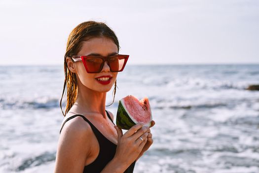 cheerful woman in sunglasses eating watermelon by the ocean. High quality photo
