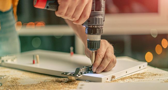 Man working with electric screwdriver and screws during process of furniture manufacturing