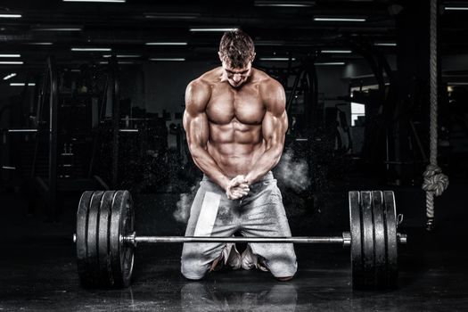 Athletic shirtless young sports man - fitness model with barbell in gym.