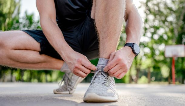 Sportive man guy sitting at the stadium outdoors and ties shoelaces on sneakers. Portrait of athlete male person during workout outdoors