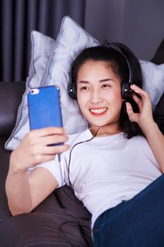 woman enjoying music in headphones, making selfie photo with cellphone while lying on sofa at home