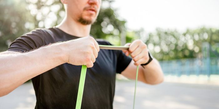 Sportive man guy training with elastic rubber band at the stadium outdoors with sunlight. Athlete male person during workout with additional sport equipmant
