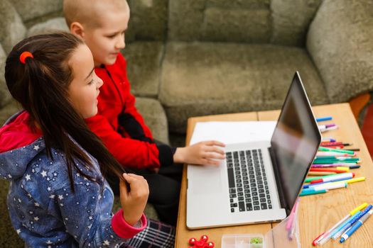 Two beautiful cute happy smiling children, a boy and a girl, use laptop for distance learning or entertainment.