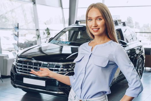 Attractive young female car dealer standing in showroom near a new car