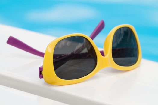 Children sunglasses lying on a deck-chair on blue water background