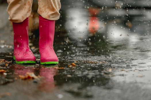 Kid wearing rubber boots standing in puddle in rainy day at autumn. Child feet in gumboots outdoors in fall season
