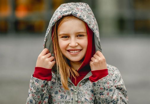 Preteen girl wearing hood and smiling at the street at autumn. Pretty female kid portrait outdoors in fall season