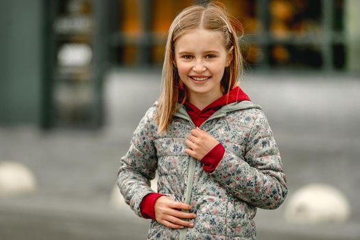 Pretty girl kid autumn portrait outdoors. Preteen female child closes coat at the street