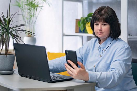 Young woman is working at her workplace. Business woman with laptop and phone in hand.