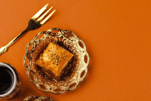 Turkish dessert baklava served on traditional metal tableware on orange background