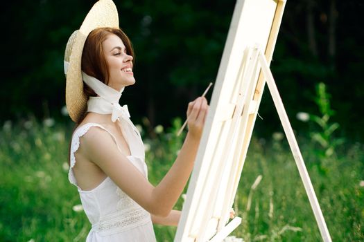 Woman in white dress paints a picture on nature easel. High quality photo