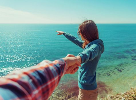 Couple in love. Beautiful young woman holding man's hand and showing him something in distance the sea. Point of view shot