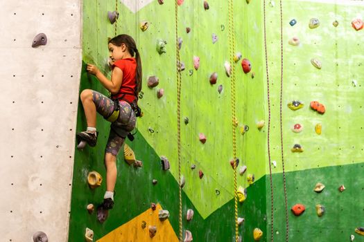 Sporty little girl climbing artificial boulder on practical wall in gym