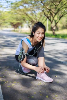 young sporty woman tying shoelaces while listening to music with earphones from her smartphone in the park 