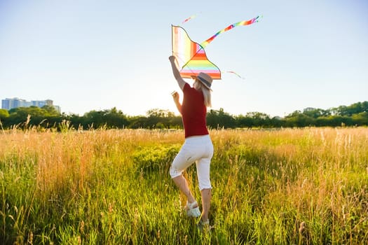 Portrait of a young and carefree woman launching kite on the greenfield. Concept of active lifestyle in nature