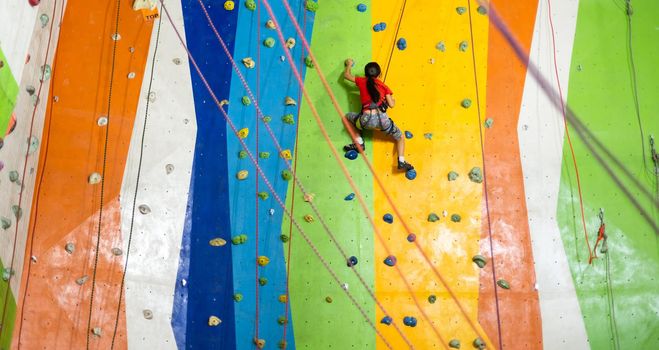 Sporty little girl climbing artificial boulder on practical wall in gym