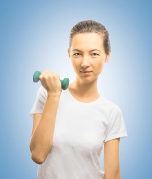 Happy young woman makes exercise with a dumbbell on a blue background