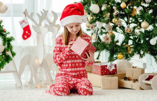 Pretty child girl holding Christmas red gift box in decorated room. Kid celebrating New Year with presents at home