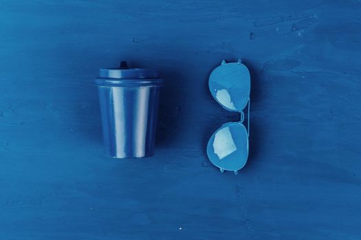 Top view of takeaway coffee cup with aviator sunglasses on classic blue background. Close up.
