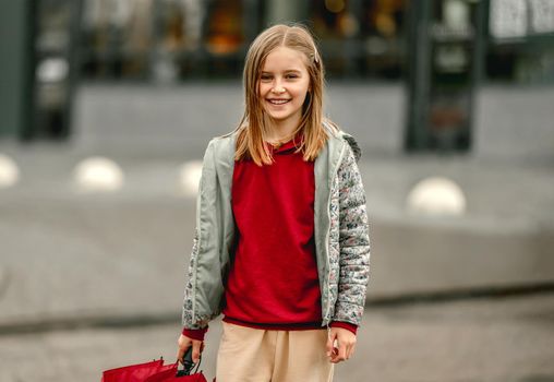 Preteen girl with umbrella in rainy evening at autumn looking at camera and smiling. Pretty kid portrait outdoors