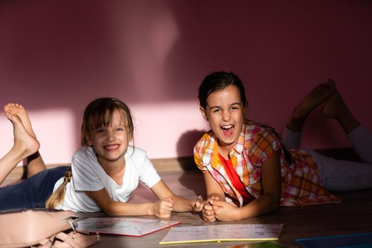 family, leisure and childhood concept - happy sisters lying on floor and doing homework at home