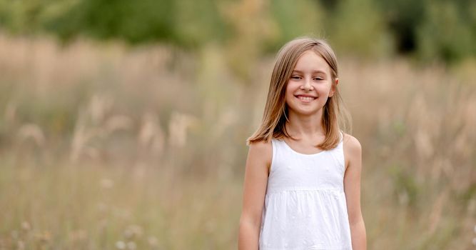 Preteen girl in the field smiling and looking at camera. Pretty child kid at the nature
