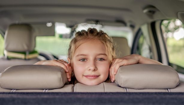 Cute preteen girl with hairstyle sitting in the car, looking at the camera and smiling. Child kid in the vehicle inside during summer trip