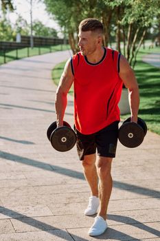 athletic man with dumbbells in his hands outdoors in the park. High quality photo