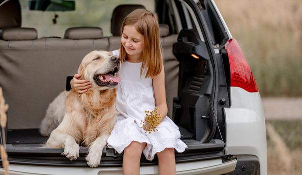 Preteen girl with golden retriever dog sitting in car trunk together. Pretty child kid hugging doggy pet in vehicle