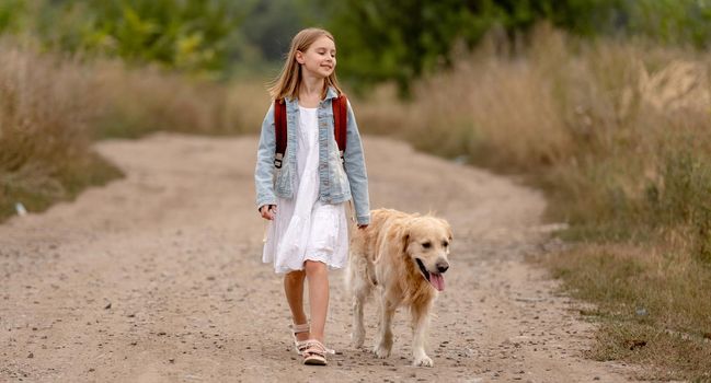 School girl and golden retriever dog walking in the field together. Preteen child kid with doggy pet and backpack at nature