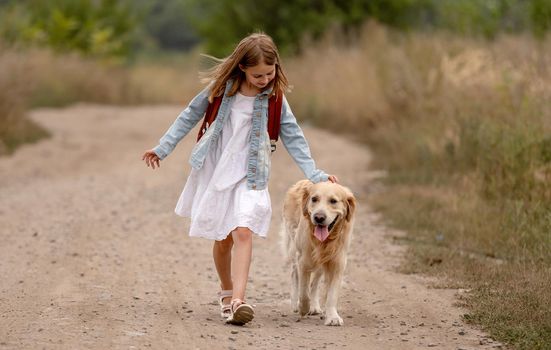 School girl with backpack and golden retriever dog running in the field. Preteen child kid with doggy pet at nature together