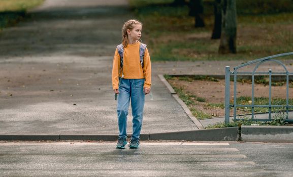 School girl with backpack outdoors walking. Pretty female child kid after lessons going home