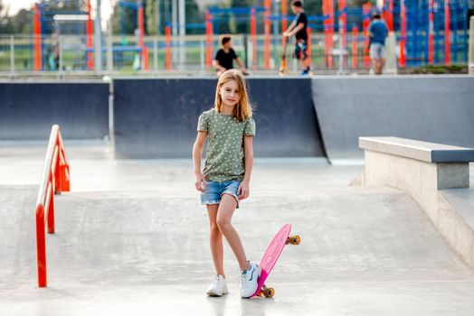 Pretty preteen girl with skateboard outdoors. Female skater child close to the park riding ramp
