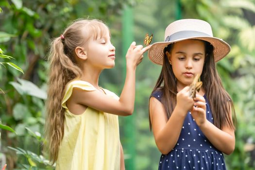 Two little sisters holding a butterfly in their hands. Children exploring nature. Family leisure with kids at summer.