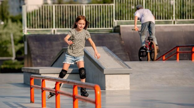 Beautiful child girl wearing roller skates riding in the park. Preteen female kid rollerblading at ramp