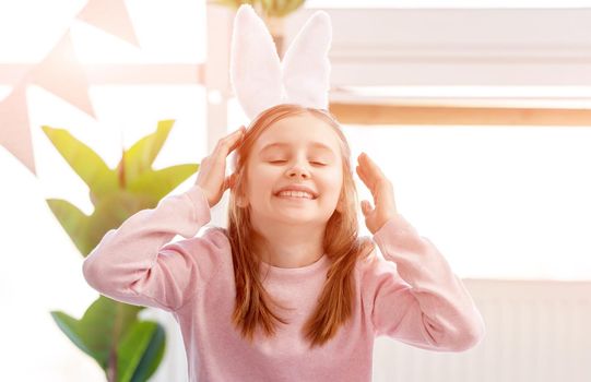 Little girl wearing bunny ears smiling in the sunny room at Easter day